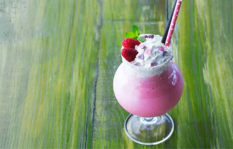 A pink raspberry milkshake topped with whipped cream and fresh strawberries, a delicious and refreshing treat.