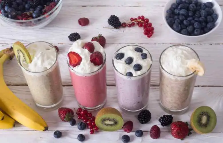 A table topped with three glasses filled with smoothies, including raspberry milkshake, ready to be enjoyed.