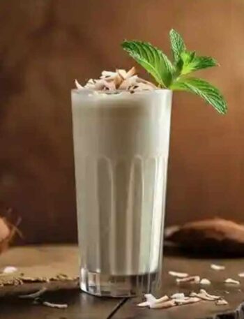 A clear glass of coconut milkshake topped with coconut flakes and mint leaves.