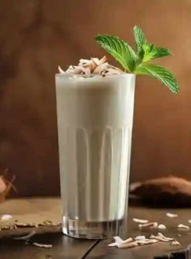 A clear glass of coconut milkshake topped with coconut flakes and mint leaves.