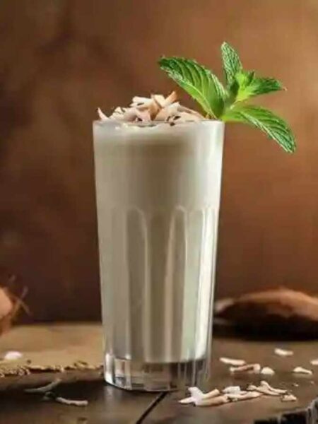 A clear glass of coconut milkshake topped with coconut flakes and mint leaves.