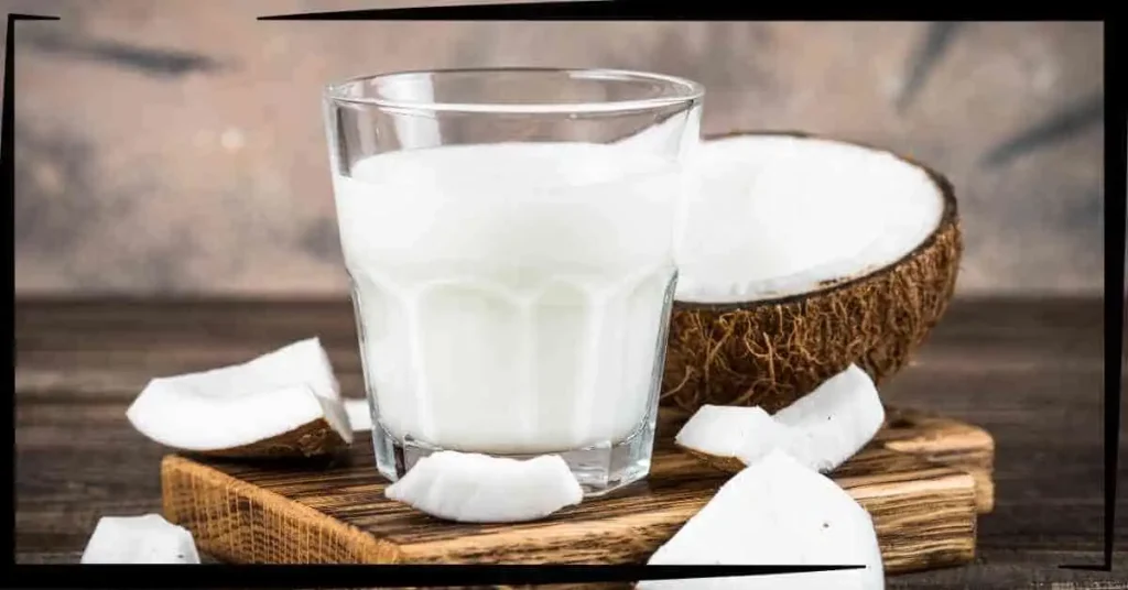 A glass of coconut milkshake next to a cut-up coconut.