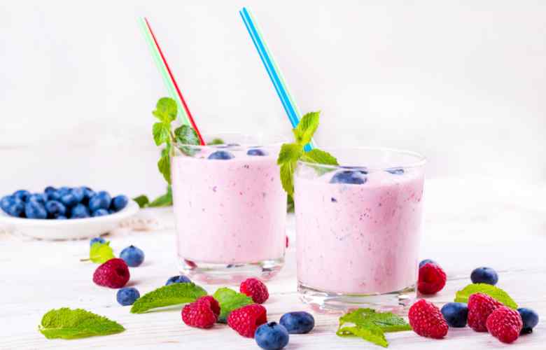 A couple of glasses filled with fruit next to a bowl of berries, perfect ingredients for a refreshing raspberry milkshake.