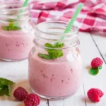 Two mason jars filled with raspberry milkshake, garnished with fresh raspberries.