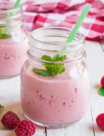 Two mason jars filled with raspberry milkshake, garnished with fresh raspberries.