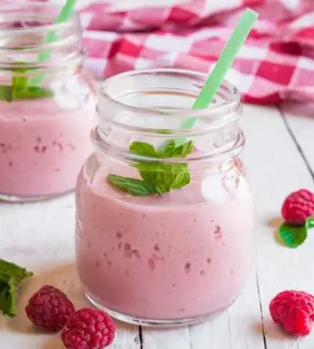 Two mason jars filled with raspberry milkshake, garnished with fresh raspberries.