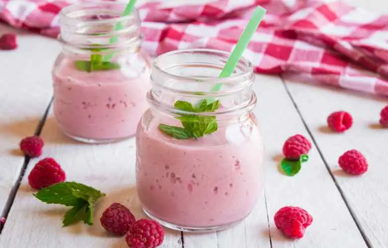 Two mason jars filled with raspberry milkshake, garnished with fresh raspberries.